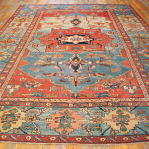 Large Persian-style rug with intricate medallions and geometric patterns in coral, blue, cream, and beige on wood flooring.