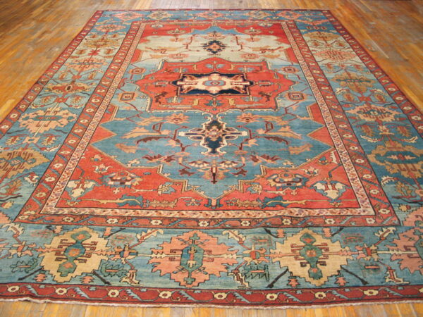 Large persian-style rug with intricate medallions and geometric patterns in coral, blue, cream, and beige on wood flooring.