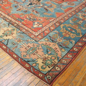 Teal and burnt orange patterned rug corner shown on worn, light brown wood planks.
