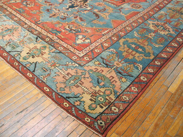 Teal and burnt orange patterned rug corner shown on worn, light brown wood planks.
