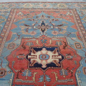 Blue and red traditional rug with a large central medallion on a light gray concrete surface.