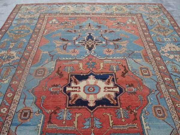 Blue and red traditional rug with a large central medallion on a light gray concrete surface.