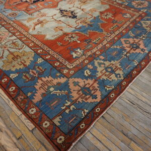 Diagonal view of a patterned rug in rust, blue, and peach colors over weathered wooden plank floors.