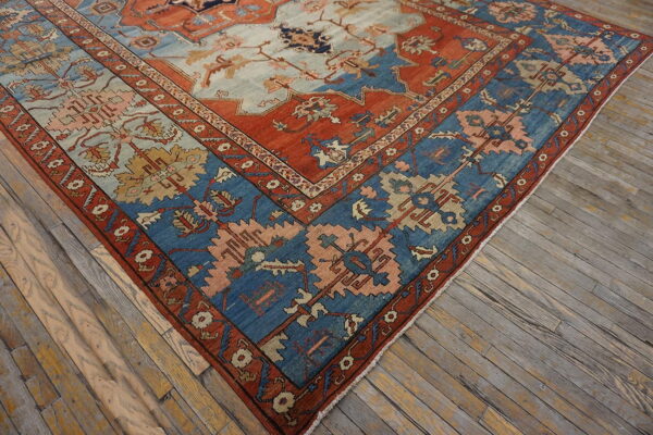 Diagonal view of a patterned rug in rust, blue, and peach colors over weathered wooden plank floors.