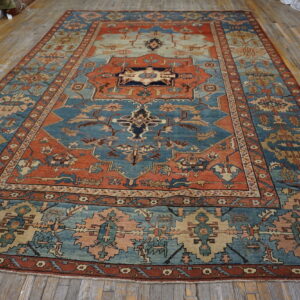 Traditional low-pile rug featuring blue, rust, and beige geometric patterns lies flat on distressed wood flooring.