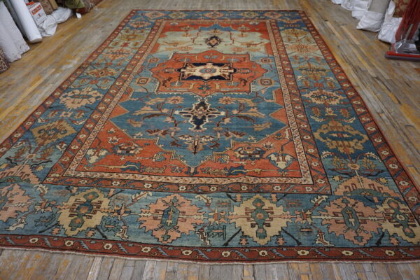Traditional low-pile rug featuring blue, rust, and beige geometric patterns lies flat on distressed wood flooring.