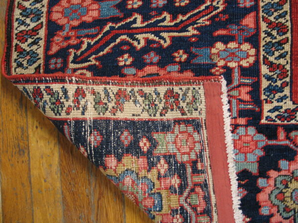 Tightly woven rug in navy, red, and cream folded back on a distressed hardwood floor.
