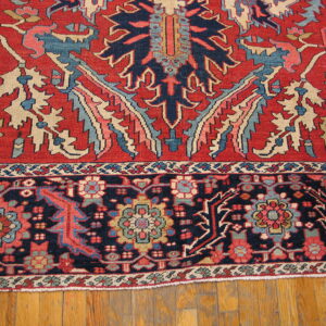 A patterned rug in red, navy blue, light blue, and beige rests on natural hardwood floorboards.