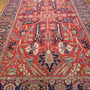 Red rug with large, stylized geometric motifs in navy blue, pink, and light blue on hardwood.