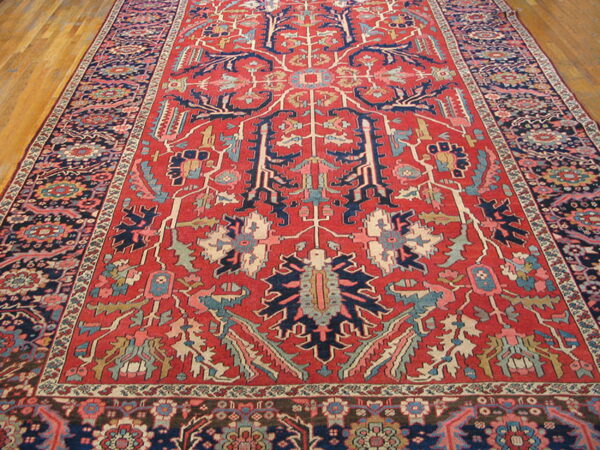 Red rug with large, stylized geometric motifs in navy blue, pink, and light blue on hardwood.