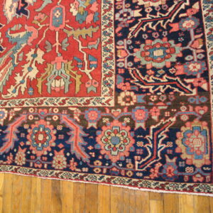 Red and navy traditional rug corner featuring detailed floral geometric patterns on wood planks.