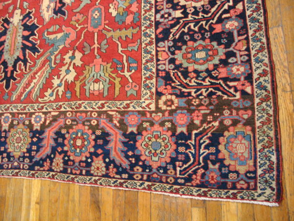 Red and navy traditional rug corner featuring detailed floral geometric patterns on wood planks.