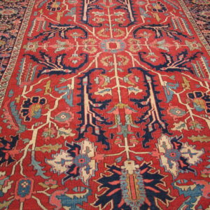 Red rug with high contrast navy and cream traditional patterns rests on light hardwood flooring.