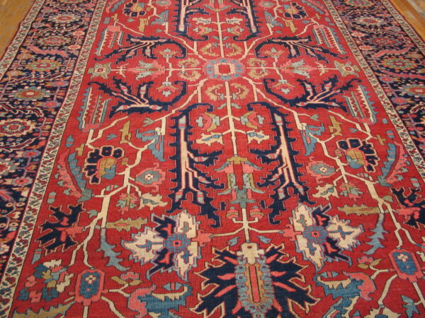 Red rug with high contrast navy and cream traditional patterns rests on light hardwood flooring.