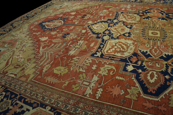 Rust-colored low pile rug with navy blue and tan geometric medallions and busy tribal patterns.