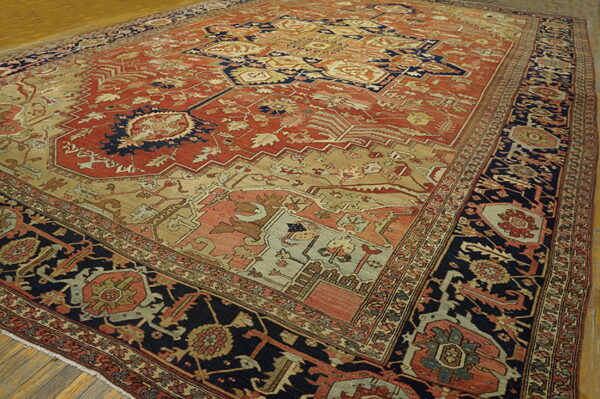 Ornate traditional rug with a rust field, deep navy border, and beige accents on wood floorboards.