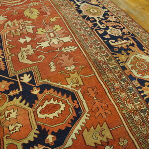 Geometric rug in rust, navy, and tan colors, showing the detailed border on hardwood flooring.