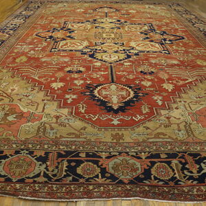 Large traditional rug in terracotta, navy, and beige with complex patterns on wooden flooring.