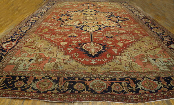 Large traditional rug in terracotta, navy, and beige with complex patterns on wooden flooring.
