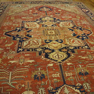 Large, low-pile rug in rust and navy with dense geometric patterns centered on light wood floors.