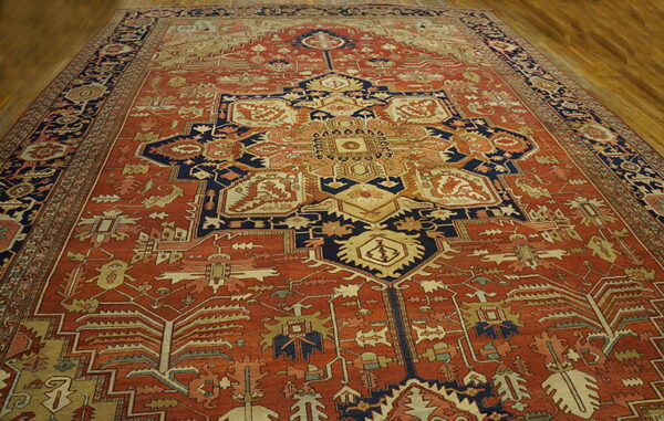 Large, low-pile rug in rust and navy with dense geometric patterns centered on light wood floors.