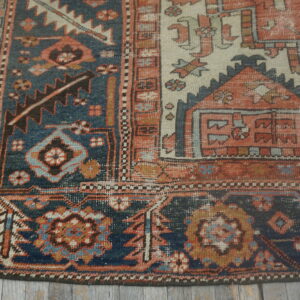 Distressed, low-pile geometric rug in indigo blue, terracotta, and cream on gray wood planks.