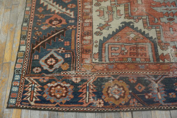 Distressed, low-pile geometric rug in indigo blue, terracotta, and cream on gray wood planks.