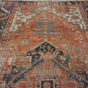 Low-pile tribal rug featuring faded rust, navy, and cream geometric patterns on wood flooring.