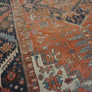 Geometric patterned rug in rust orange, navy, and light blue rests on distressed wood flooring.