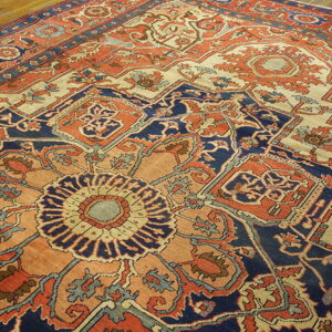A low pile, traditional rug featuring a detailed medallion pattern in navy, coral, and cream on wood floor.