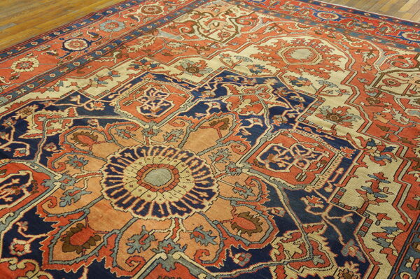 A low pile, traditional rug featuring a detailed medallion pattern in navy, coral, and cream on wood floor.