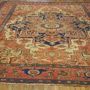 Ornate traditional rug in coral, cream, and navy blue with a central medallion on hardwood floors.