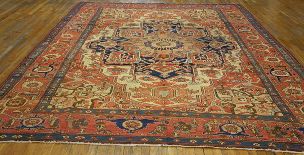 Ornate traditional rug in coral, cream, and navy blue with a central medallion on hardwood floors.