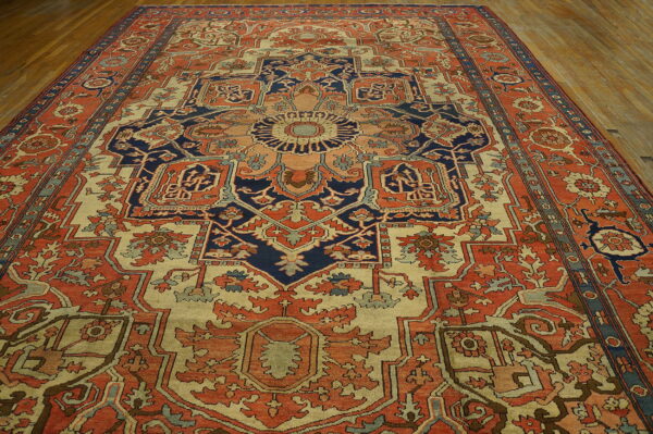 A large medallion rug in coral, cream, and deep blue sits on polished wood flooring.