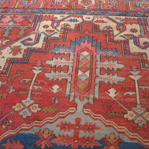 Close view of a geometric rug pattern primarily in rust red, cream, and dusty blue.