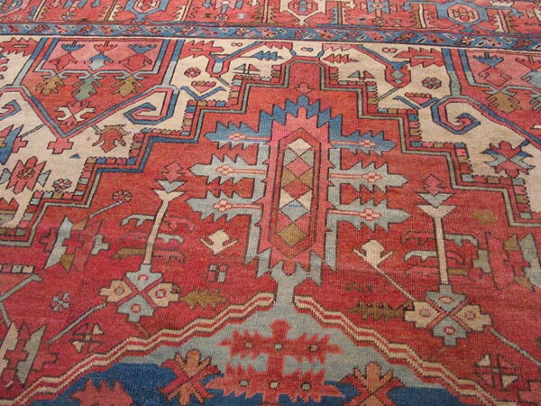 Close view of a geometric rug pattern primarily in rust red, cream, and dusty blue.