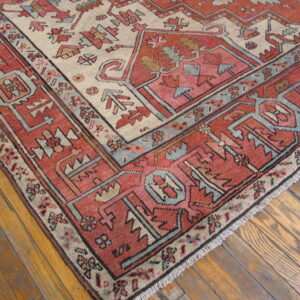 Close-up of a geometric rug in red, pink, cream, and blue on rustic wood flooring.