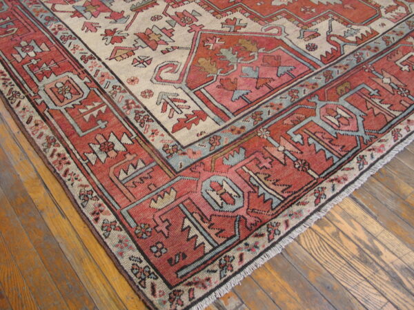 Close-up of a geometric rug in red, pink, cream, and blue on rustic wood flooring.