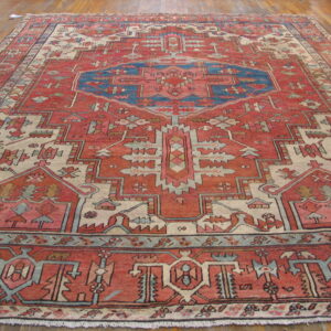 A large geometric rug in shades of red, blue, and cream covers wood plank flooring.