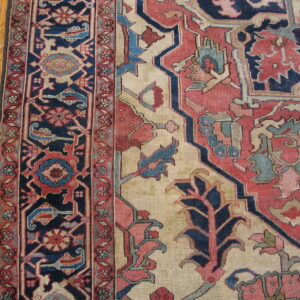 Intricate low-pile rug featuring navy, rose, and cream traditional motifs, bordered by light wood flooring.