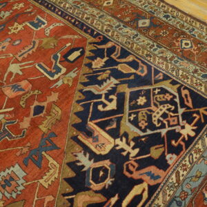 Red field and navy corner with stylized, angular tribal patterns, bordered by wood flooring.