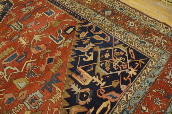 Red field and navy corner with stylized, angular tribal patterns, bordered by wood flooring.