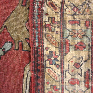 Low-pile rug detail showing geometric patterns in strong red, tan, khaki, and dark blue fibers.