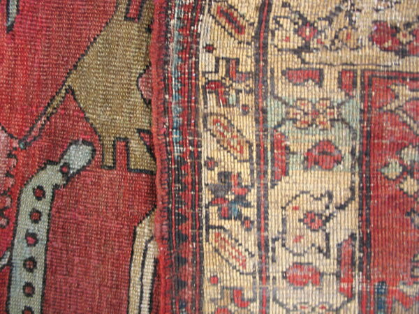 Low-pile rug detail showing geometric patterns in strong red, tan, khaki, and dark blue fibers.