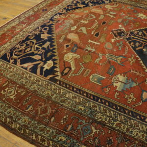 Geometric red and dark blue rug featuring stylized motifs and multiple borders on a light wood floor.