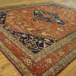 Distressed, low-pile rug featuring a navy medallion on a terracotta field with complex folk motifs on wood flooring.