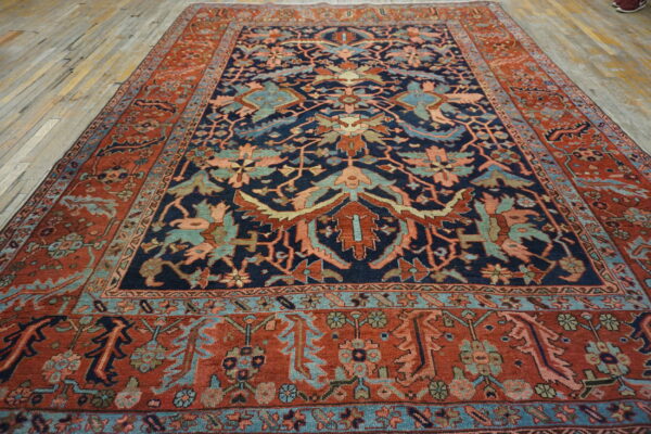 Low pile rug with navy blue, rust, and teal complex motifs sits on aged light wood flooring.