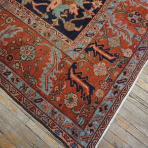 Rust and navy patterned rug with teal borders rests diagonally on gray, weathered wood flooring.