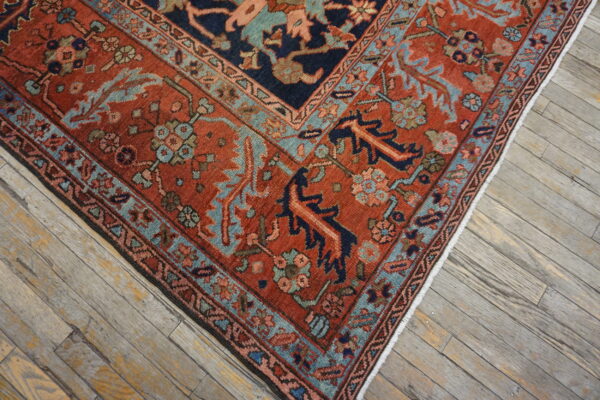 Rust and navy patterned rug with teal borders rests diagonally on gray, weathered wood flooring.