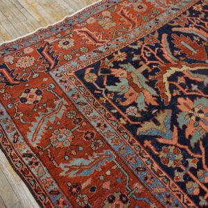 Navy and rusty red patterned rug with light blue borders rests on distressed wood planks.